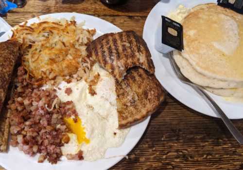 A hearty breakfast plate with eggs, hash browns, bacon, toast, and a side of pancakes.