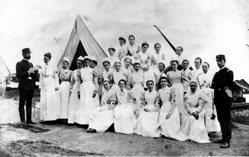 A historical black-and-white photo of a group of nurses in white uniforms, posing outside a tent.