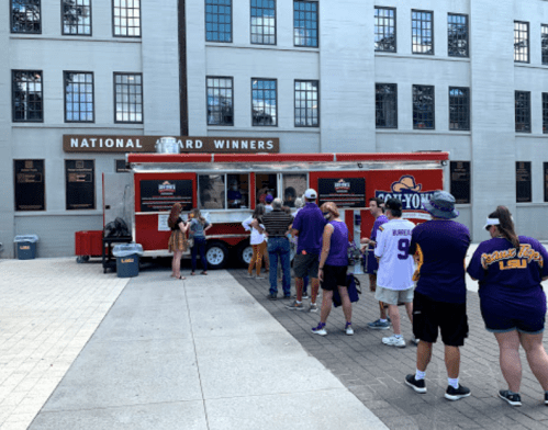 A food truck with a line of people in purple attire outside a building labeled "National Award Winners."