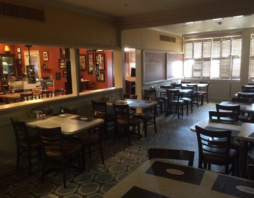 A cozy restaurant interior with empty tables, wooden chairs, and warm lighting, featuring a patterned floor.