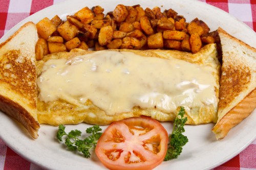 A plate featuring a cheese omelet, golden-brown potatoes, toast, and a slice of tomato, on a checkered tablecloth.
