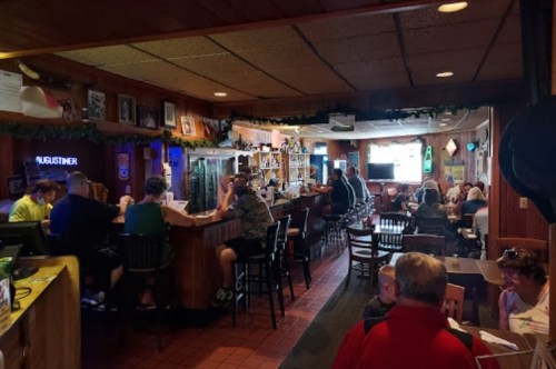 A cozy bar scene with patrons seated at the counter and tables, surrounded by wooden decor and a lively atmosphere.