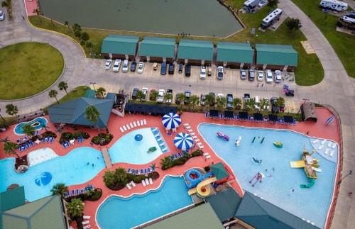 Aerial view of a vibrant pool area with water slides, lounge chairs, and nearby parked vehicles.