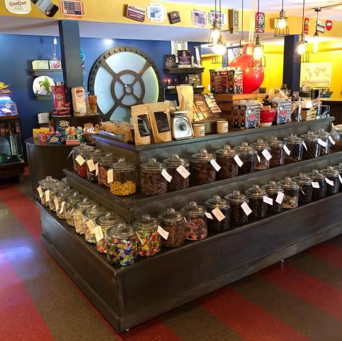 A colorful candy shop display featuring jars of various candies on wooden shelves, with a vintage decor.
