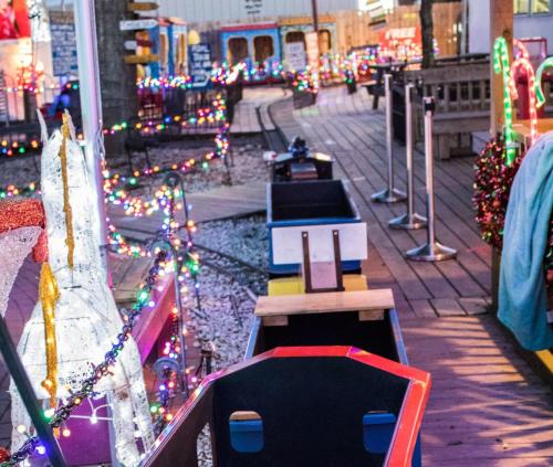 Colorful holiday lights adorn a festive pathway with a decorated horse statue and empty train cars.