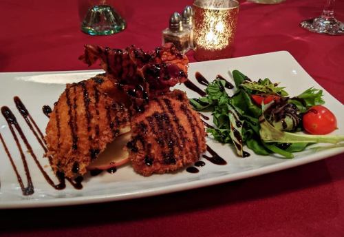 A plated dish featuring grilled chicken, drizzled with sauce, alongside a fresh salad and cherry tomatoes on a red tablecloth.