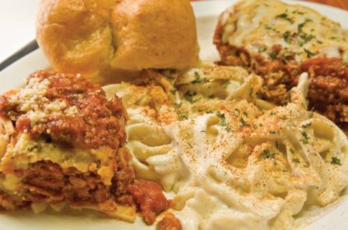 A plate of pasta with marinara sauce, creamy fettuccine, and two bread rolls, garnished with herbs.