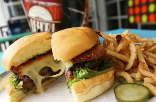 Two burgers with melted cheese and lettuce, served with crispy fries and pickles on a blue plate.