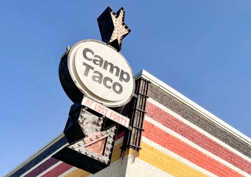 Sign for Camp Taco at Lost Forty, featuring a star and colorful striped building under a clear blue sky.