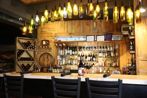 A cozy bar with wooden decor, illuminated by hanging bottle lights, showcasing a variety of spirits and wine.