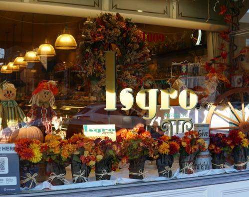 A storefront decorated with autumn flowers, pumpkins, and scarecrows, featuring the name "Isgro" prominently displayed.