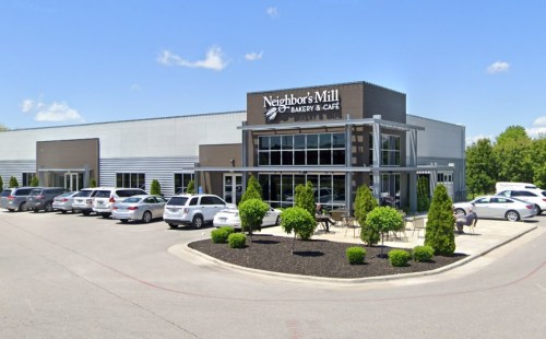 Exterior of Neighbor's Mill Bakery & Café, featuring a modern building, parked cars, and landscaped greenery.