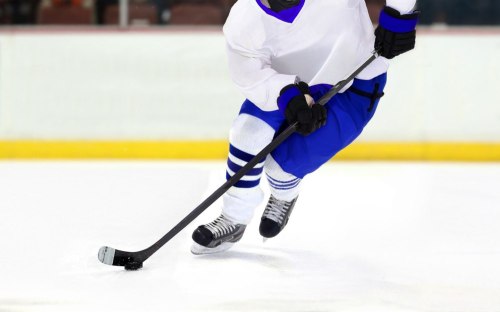 A hockey player in a white jersey and blue shorts skating on ice while handling a puck with a stick.