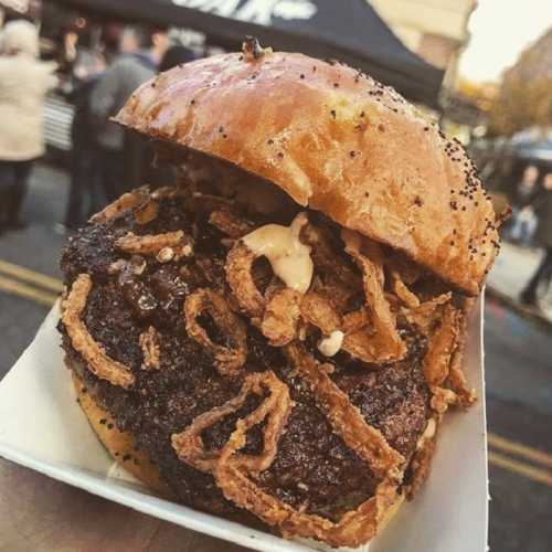 A close-up of a juicy burger topped with crispy fried onions, served in a toasted bun.