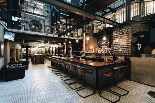 A stylish bar interior with a long wooden counter, high stools, and industrial decor, featuring a well-stocked back bar.