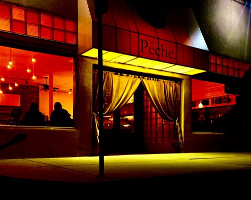 A warmly lit restaurant entrance with a curtain, glowing orange lights, and a sign reading "Pêche."
