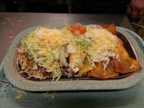A platter of crispy tacos topped with shredded lettuce, cheese, and diced tomatoes on a green tray.