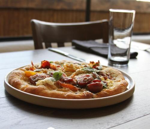 A freshly baked pizza topped with vegetables and herbs, served on a plate, with a glass of water in the background.