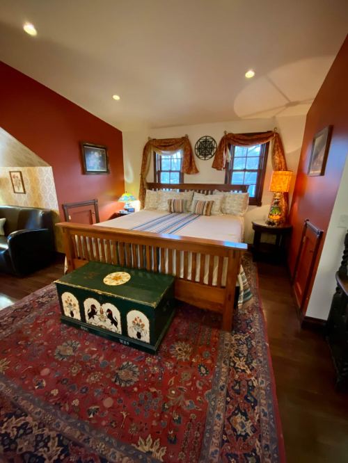 Cozy bedroom with a large bed, decorative rug, wooden furniture, and warm lighting against a red wall.