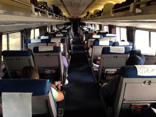 Interior view of a train carriage with rows of seats and passengers sitting quietly, some reading or using devices.