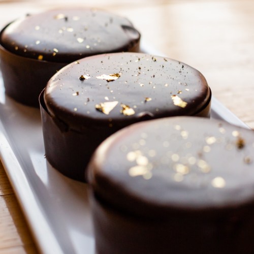 Three round chocolate desserts topped with gold leaf, arranged on a white platter.