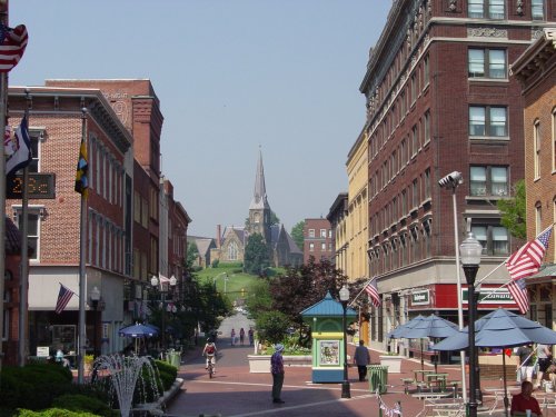 A view of a charming street lined with buildings, leading to a church with a tall spire in the background.