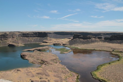 A panoramic view of a desert landscape with a winding river and rocky cliffs under a clear blue sky.