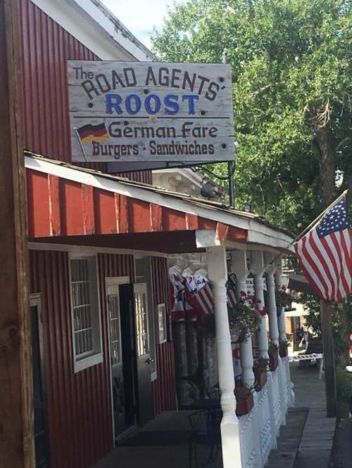 Sign for "The Road Agents Roost" featuring German fare, burgers, and sandwiches, with an American flag in the foreground.