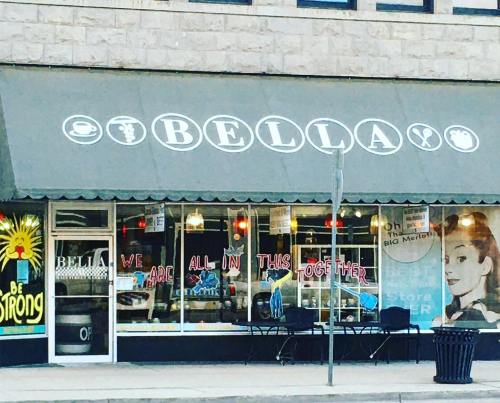 A café named "Bella" with a welcoming sign and outdoor seating, featuring a mural of a woman and a motivational message.