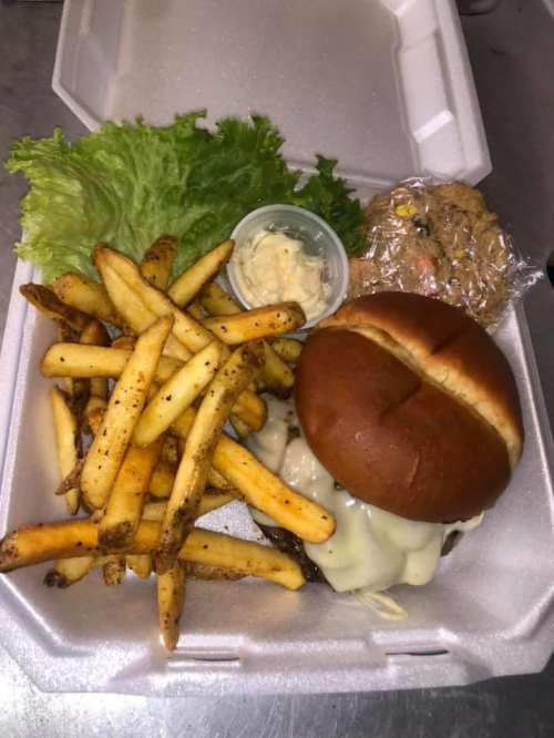 A takeout container with a cheeseburger, fries, lettuce, a small dessert, and a cup of sauce.