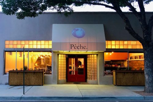 Exterior of a restaurant named "Pêche," featuring a red door and warm lighting, surrounded by trees.
