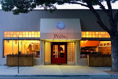 Exterior of a restaurant named "Pêche," featuring a red door and warm lighting, surrounded by trees.