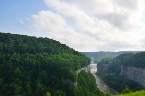 A scenic view of a lush green canyon with a river flowing through it, under a partly cloudy sky.