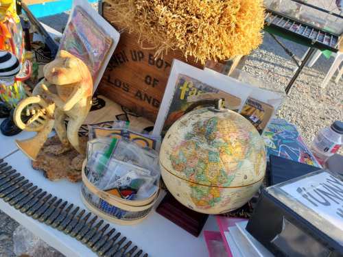 A cluttered table with a globe, vintage magazines, decorative items, and various trinkets.