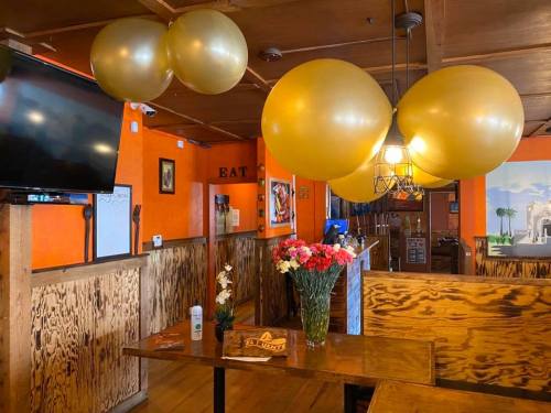 A cozy restaurant interior with orange walls, gold balloons, a floral centerpiece, and a TV on the wall.