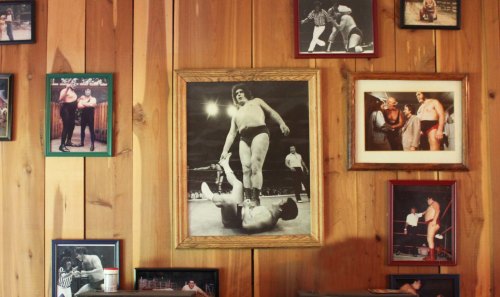 A wooden wall adorned with various framed wrestling photos, featuring a prominent black-and-white image of a wrestler.