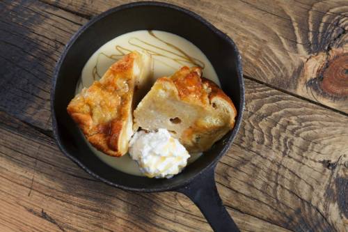 A cast iron skillet with two pieces of dessert, drizzled with sauce and a dollop of whipped cream on a wooden surface.
