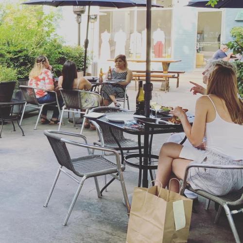 A group of people sitting at outdoor tables, enjoying drinks and conversation in a sunny setting.