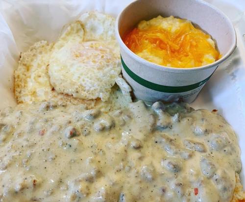 A plate featuring two fried eggs, creamy sausage gravy, and a cup of cheesy grits.