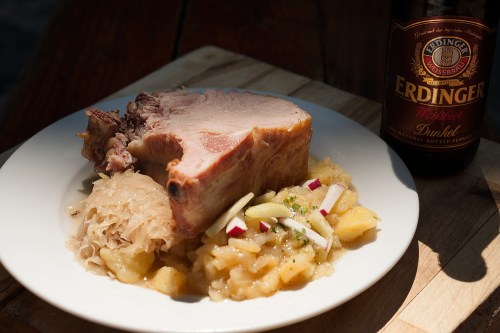 A plate of pork with sauerkraut and apple sauce, accompanied by a bottle of Erdinger Dunkel beer.