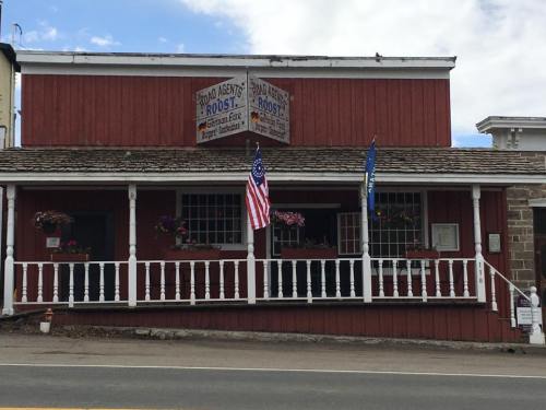 A red wooden building with a porch, featuring flower boxes and American flags, labeled "Roost" and "Agent's Roost."