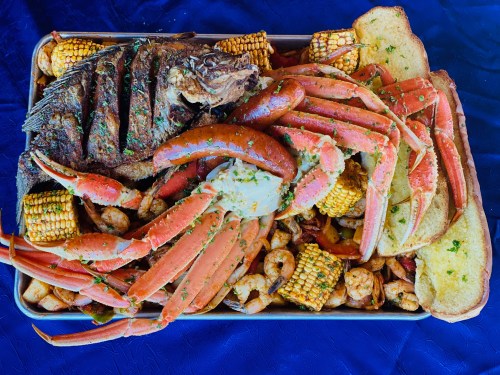 A vibrant seafood platter featuring crab legs, shrimp, grilled fish, corn, sausage, and toasted bread.