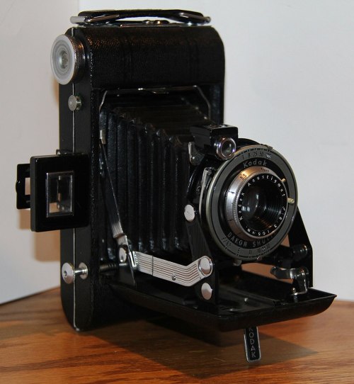 A vintage Kodak folding camera with a black leather exterior and a bellows design, resting on a wooden surface.
