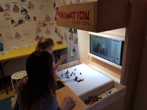 Two children interact with an animation station, creating stop-motion animations with small figures and a screen display.
