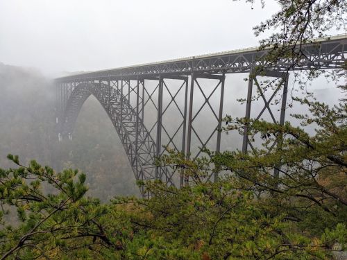 A large steel bridge arches over a misty landscape, surrounded by trees and fog.