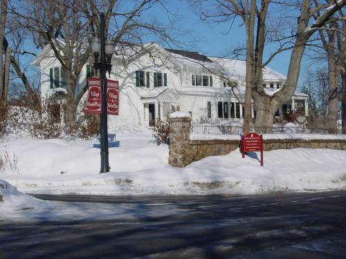 A large white house surrounded by snow, with trees and street signs visible in a winter landscape.
