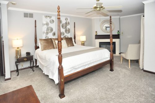 A spacious bedroom featuring a four-poster bed, soft lighting, and a cozy seating area with a fireplace.