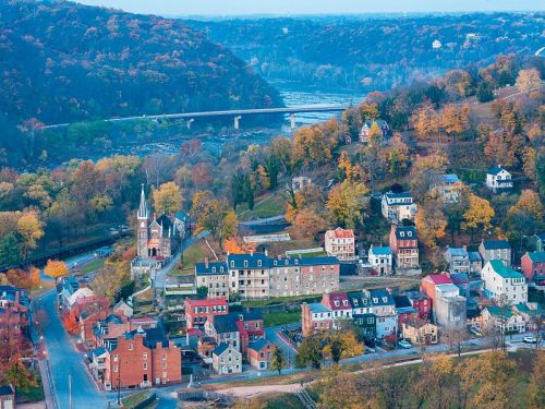 Aerial view of a quaint town with colorful autumn foliage, a river, and a bridge in the background.