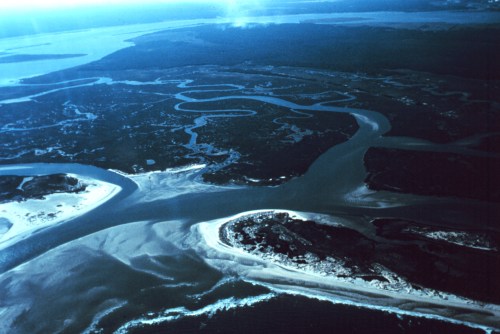 Aerial view of a winding river system with islands and sandy shores, surrounded by lush greenery and water.