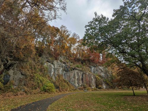 A rocky cliff surrounded by autumn trees, with a winding path in a park setting.